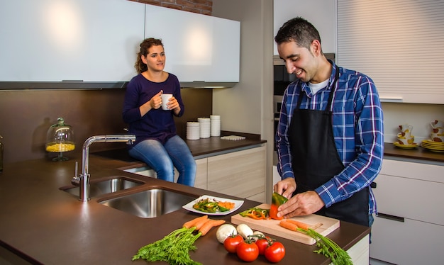 Couple parlant dans la cuisine pendant que le mari coupe des légumes pour préparer à manger