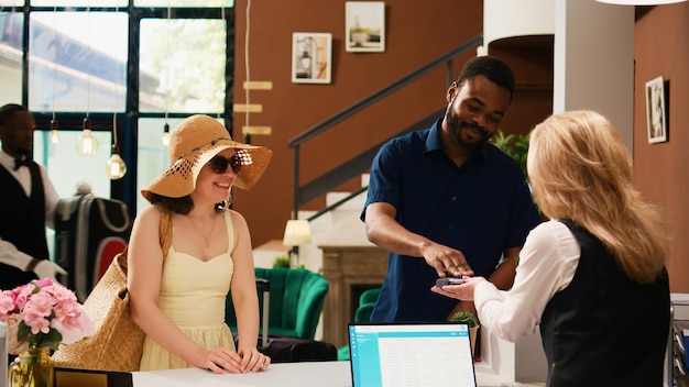 Couple payant l'hébergement à l'enregistrement, effectuant le paiement au terminal POS pour profiter des vacances d'été. Touristes voyageant en lune de miel dans une station balnéaire tropicale, réception.