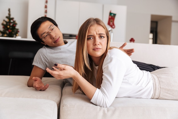Couple perplexe, homme et femme se disputant, tout en étant couchés ensemble dans son lit dans l'appartement