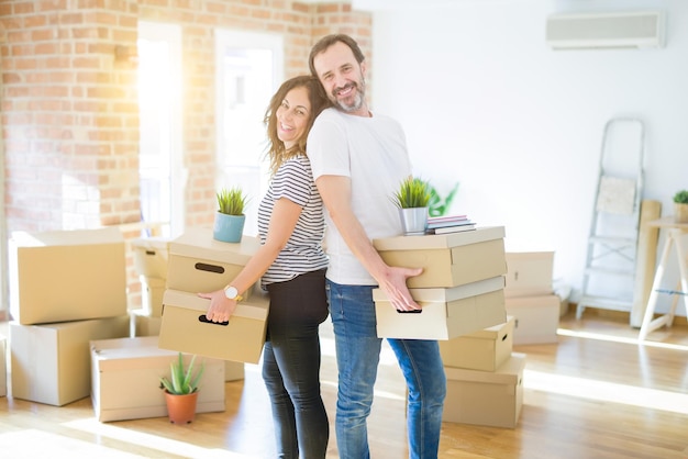 Photo couple de personnes âgées d'âge moyen déménageant dans une nouvelle maison tenant une boîte en carton souriant heureux amoureux d'un appartement