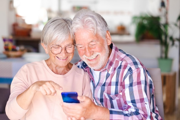 Couple de personnes âgées en appel vidéo via téléphone mobile Joyeux et souriant beau couple de personnes âgées à l'intérieur étant de bonne humeur tenant un smartphone