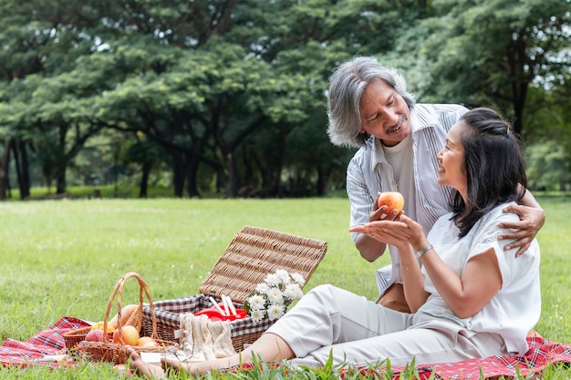 Couple de personnes âgées asiatiques relaxant et pique-nique au parc. Femme donne une pomme à mon mari.