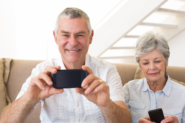 Couple de personnes âgées assis sur le canapé en utilisant leurs smartphones