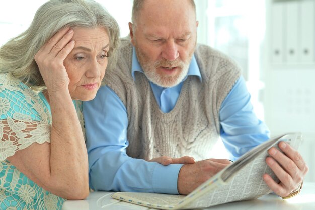 Couple de personnes âgées assis à table et lisant le journal