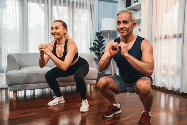Couple de personnes âgées athlétiques et sportives s'engageant dans une séance d'entraînement de jour pour les jambes avec des squats ensemble à la maison comme concept de mode de vie corporel sain après la retraite