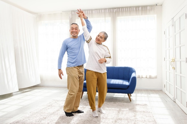 Un couple de personnes âgées bien-être asiatique romantique et joyeux aime danser et se tenir la main sur de la musique avec des sourires et du bonheur dans le salon Activité de retraite pour personnes âgées à la maison