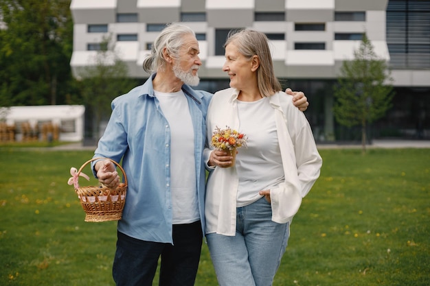 Couple de personnes âgées debout sur une herbe en été avec panier de paille et fleurs