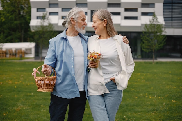 Couple de personnes âgées debout sur une herbe en été avec panier de paille et fleurs