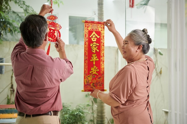 Couple de personnes âgées décorant la maison avec des distiques avec des souhaits de chance et de prospérité pour le nouvel an
