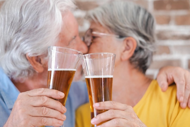 Couple de personnes âgées défocalisé s'embrassant tenant deux verres de bière fond de mur de briques