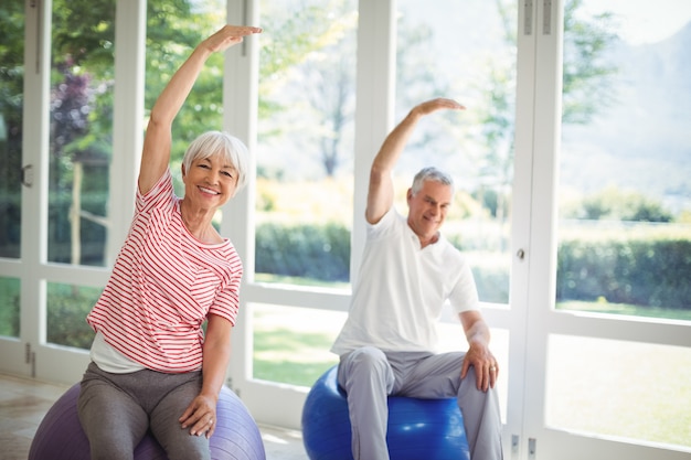 Couple de personnes âgées effectuant des exercices d'étirement sur ballon de fitness