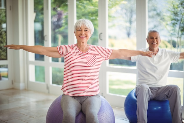 Couple de personnes âgées effectuant des exercices d'étirement sur ballon de fitness