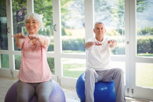 Couple de personnes âgées effectuant des exercices d'étirement sur ballon de fitness