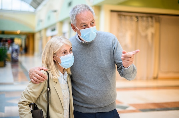 Couple de personnes âgées faisant du shopping dans un centre commercial à l'époque des coronavirus, portant des masques