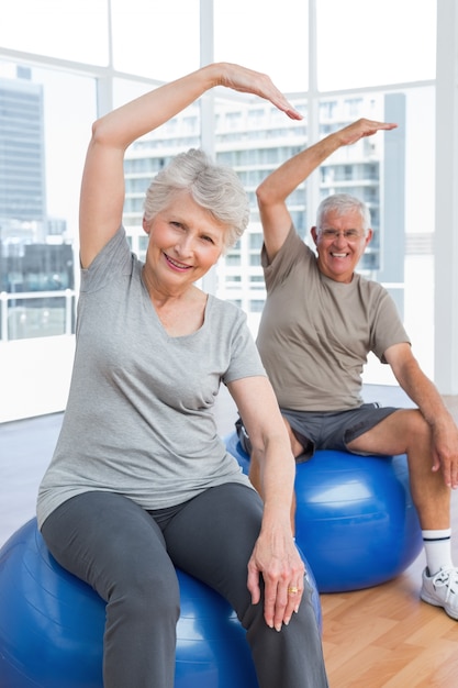 Couple de personnes âgées faisant des exercices d&#39;étirement sur des ballons de remise en forme