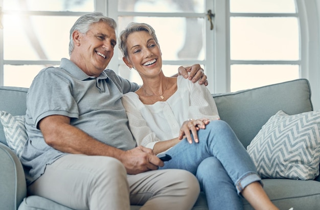 Un couple de personnes âgées heureux s'embrasse et regarde la télévision pour se divertir, se détendre ou passer du temps ensemble à la maison