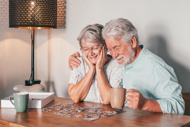 Un couple de personnes âgées insouciantes à la maison passent du temps ensemble à faire un puzzle sur la table en bois.