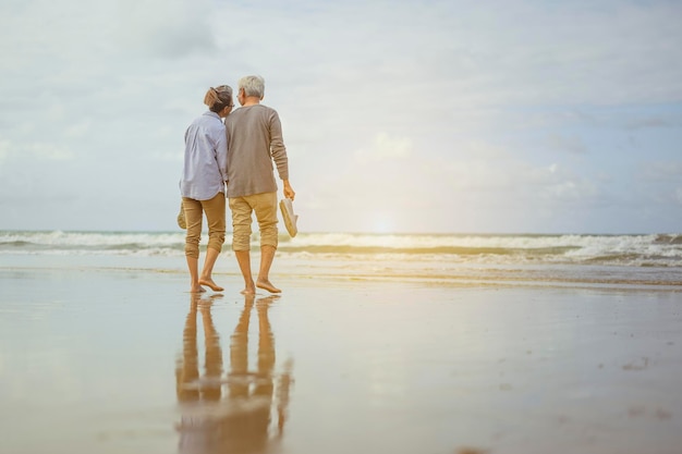 Couple de personnes âgées marchant sur la plage main dans la main au lever du soleil, plan d'assurance-vie au concept de retraite.