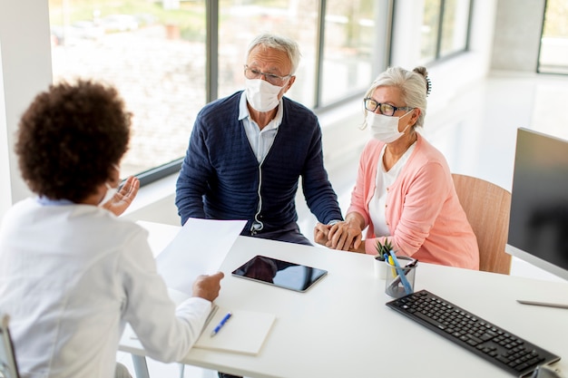 Un couple de personnes âgées avec des masques faciaux de protection reçoit des nouvelles d'une femme médecin noire au bureau