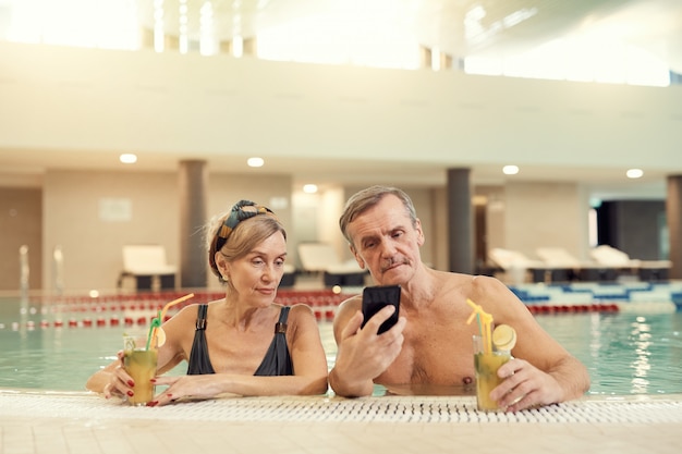 Couple de personnes âgées modernes à l'aide de Smartphone dans la piscine