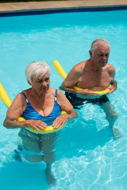 Couple de personnes âgées nageant dans la piscine avec des tubes gonflables sur une journée ensoleillée