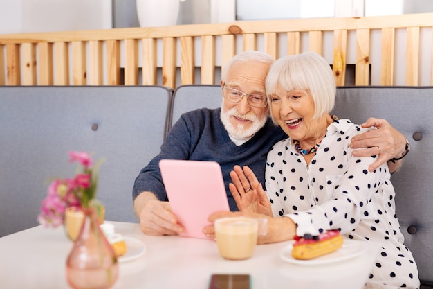 Couple de personnes âgées optimiste appliquant la tablette et la femme agitant la main