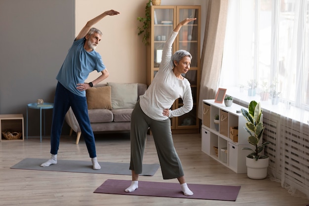 Couple de personnes âgées pratiquant le yoga à la maison