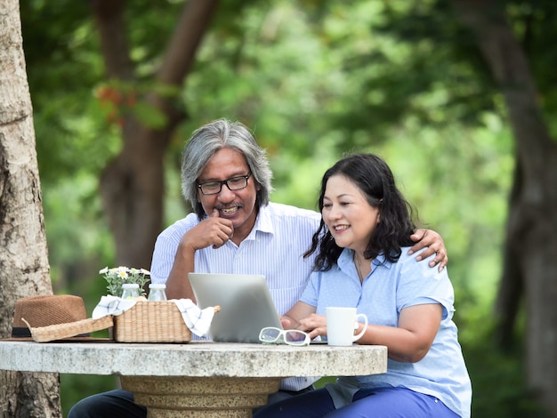 Couple de personnes âgées à la recherche d&#39;un ordinateur portable et prendre le petit déjeuner dans le jardin ensemble.