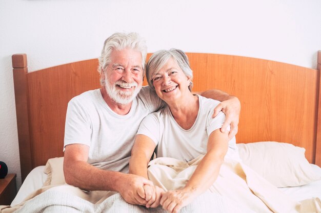 Couple De Personnes âgées Regardant Et Souriant Avec Amour Et Affect Pendant Qu'elle L'embrasse - Adultes Retraités Et Matures Mariés Dans La Chambre Le Matin Avant De Se Lever