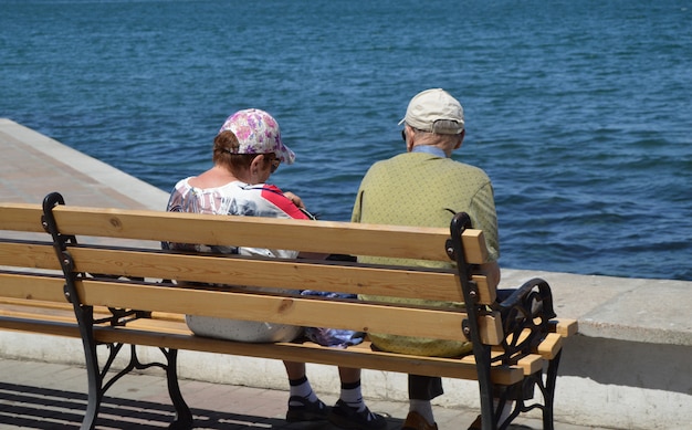 Un couple de personnes âgées regarde la mer, assis sur un banc. Le concept de récréation