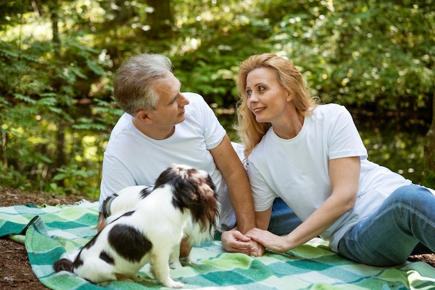 Un couple de personnes âgées se détend sur un pique-nique dans les bois et joue avec un chien sur une couverture