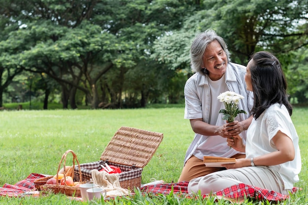 Couple de personnes âgées se détendre et pique-niquer au parc. Femme donne des fleurs à mon mari.