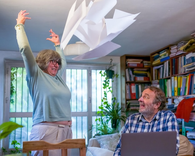Couple de personnes âgées se disputant à la maison, problèmes financiers dans la famille, femme en colère avec un homme jetant des feuilles de papier en l'air pour un accès de colère