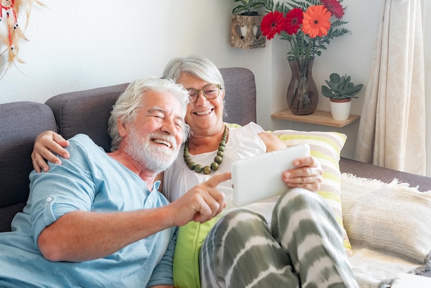 Couple de personnes âgées souriant allongé sur un canapé en utilisant ensemble des concepts de tablette numérique sur la technologie