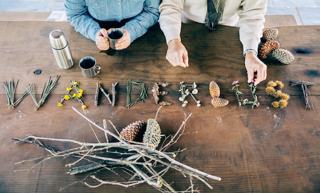 Couple de personnes âgées tenant des tasses à café et faisant un mot d'envie d'errance avec des objets naturels sur une table en bois