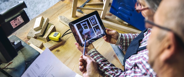 Couple de personnes âgées travaillant dans un atelier de menuiserie à la recherche d'une tablette avec chaise design