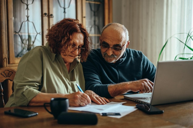 Couple de personnes âgées utilisant un ordinateur portable tout en faisant leurs finances à la maison