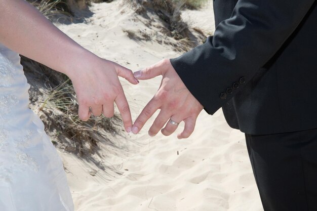 Couple sur la plage en robe de mariée en forme de coeur avec les mains