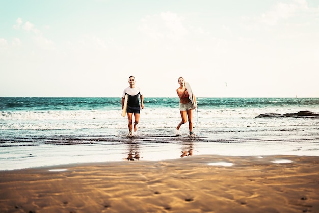 Un couple avec une planche de surf se promène sur la plage contre le ciel.