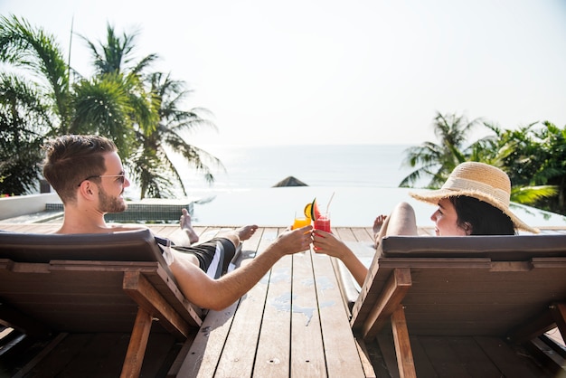 Couple portant un toast avec des cocktails au bord de la piscine