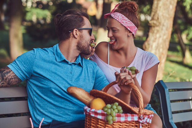 Couple portant des vêtements décontractés pendant les rencontres, pique-niquer à l'extérieur sur un banc dans le parc.