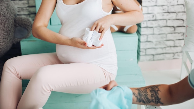 Couple de positivité de bel homme et jolie femme enceinte blonde assis dans les escaliers au studio embrassant l'estomac et gesticulant le cœur par les mains Jeune famille élégante à l'intérieur de la menthe douce parmi les jouets