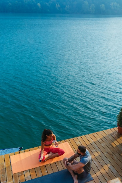 Couple pratiquant des poses de yoga dans la nature à la jetée du lac