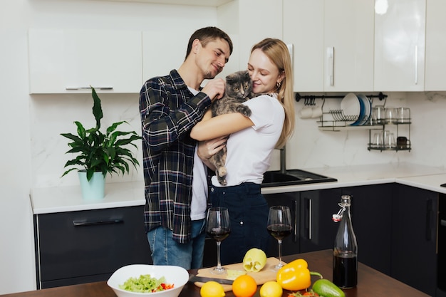 Couple prépare un dîner sain dans la cuisine femme tient un chat dans ses bras