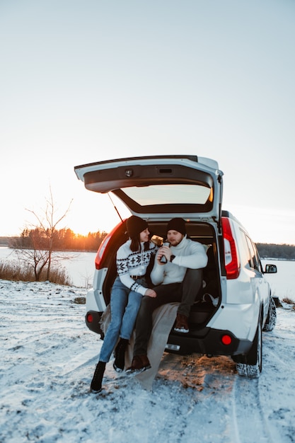 Couple près de la voiture au coucher du soleil d'hiver copie espace flou