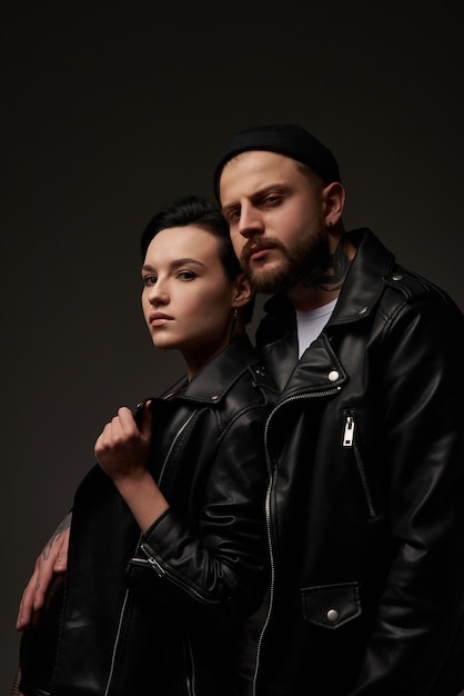 Couple punk élégant et sexy sur un fond sombre de studio dans des vestes en cuir dans des tatouages la jeune fille a des lunettes rouges