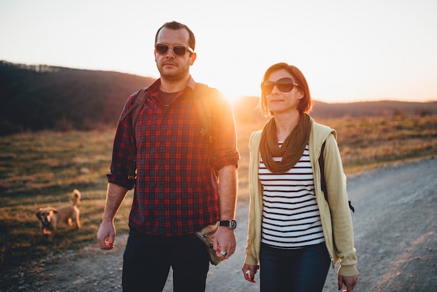 Couple de randonnée avec chien sur un chemin de terre au coucher du soleil