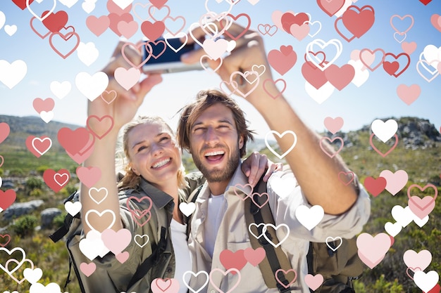 Couple de randonnée debout sur un terrain de montagne prenant un selfie contre la conception du coeur de la Saint-Valentin