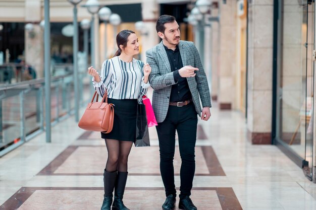 Couple à la recherche moderne dans un centre commercial, ils regardent et pointent vers la vitrine