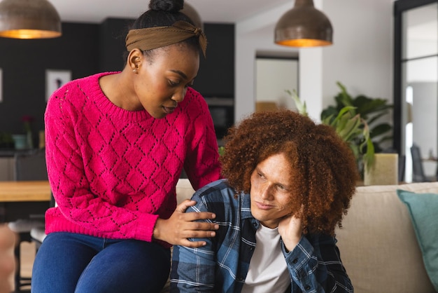 Photo un couple réfléchi, triste et diversifié assis dans le salon à la maison, s'embrassant et se réconfortant. dépression, santé mentale, relation, soutien, unité, style de vie et vie domestique, inchangés.